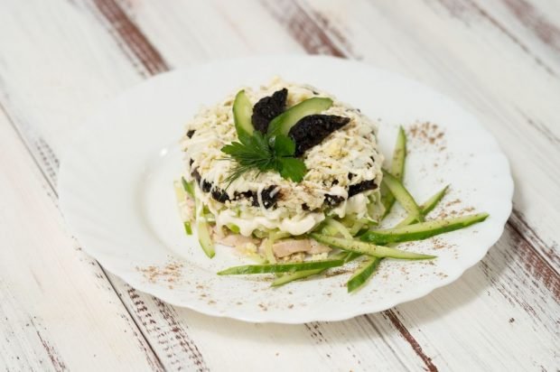 Layered salad of ham, prunes, cheese and cucumbers 